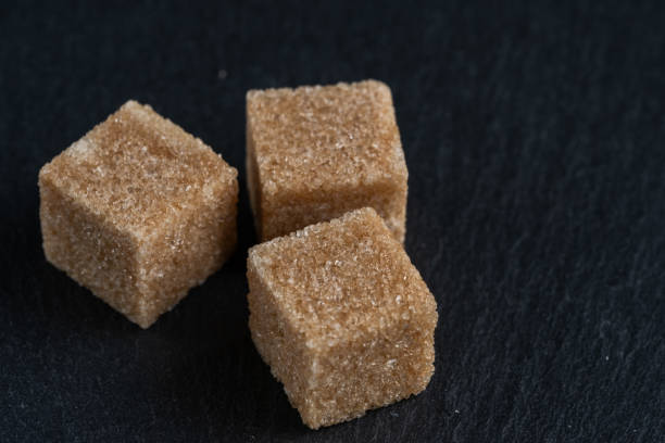 Brown cane sugar cubes on dark stone background, closeup