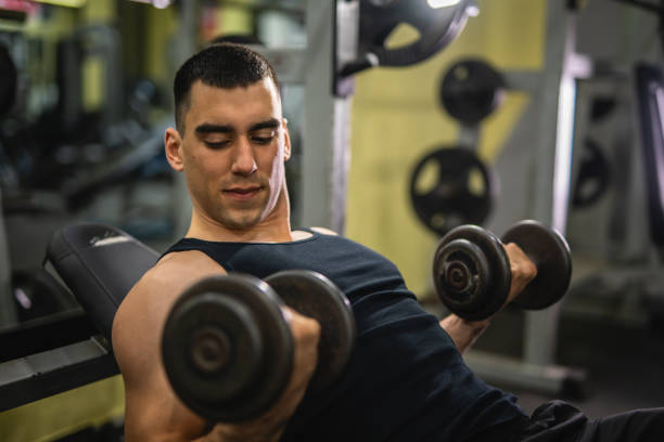 istock muscular man do exercise for biceps with dumbbells on sports bench 2197648535