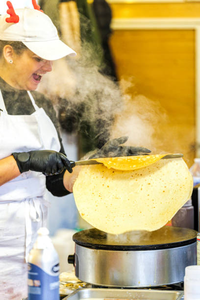 Saint-Jean-de-Luz, France - February 3, 2025: A cook preparing a crepe on an electric crepe maker at a market stall.