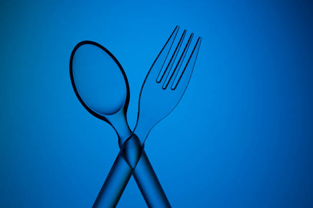 Transparent plastic crossed spoon and fork shot on deep blue background with a levitation effect