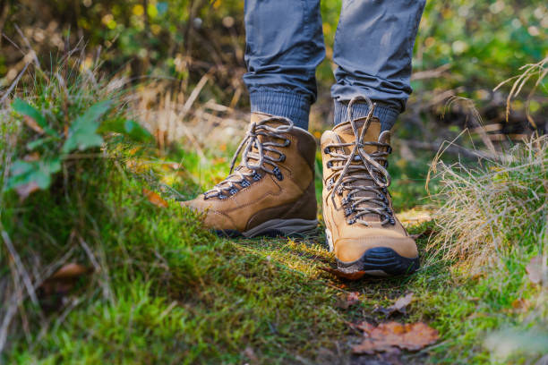 Hiker in brown trekking boots with tied stand on mossy hiking trail in forest
