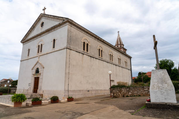 Large church with bell tower, in front view cross on stone pillar, Olib island in Zadar basin, Croatia