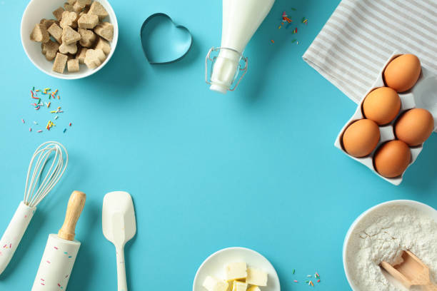 istock Baking essentials on a blue background: eggs, flour, butter, milk, sugar cubes, whisk, rolling pin, spatula, heart-shaped cookie cutter. Perfect for culinary and baking themes 2197658010