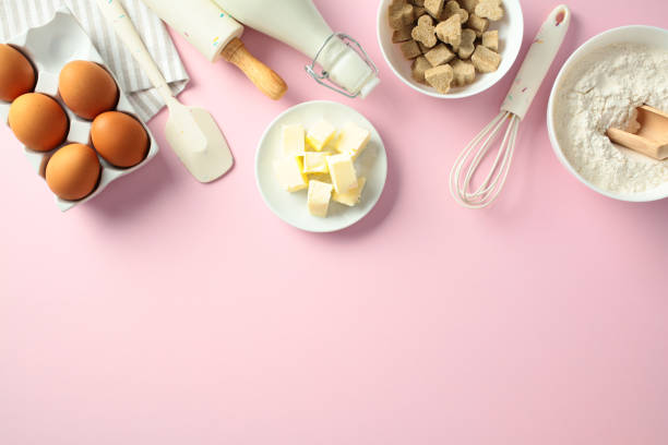 istock Baking ingredients on a pink background: eggs, butter, flour, brown sugar cubes, milk, and kitchen tools. Flat lay, top view 2197658433