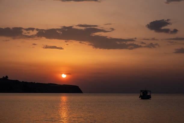Sunset with rich colours over sea and Greek coastline with a fishing boat