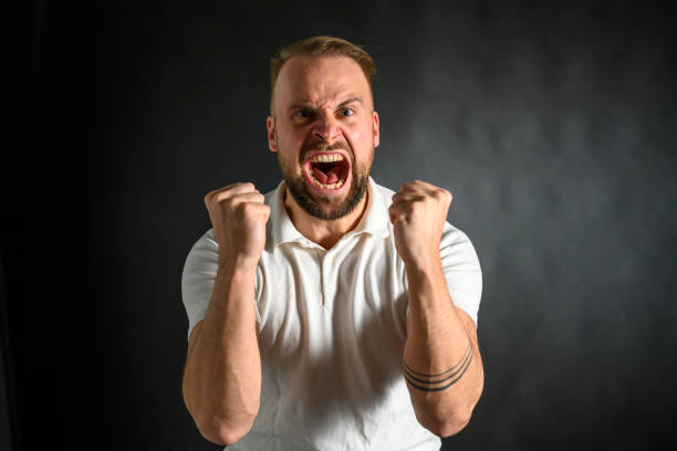 Low angle closeup studio portrait of young Caucasian man expressing feeling of wrath, gray background