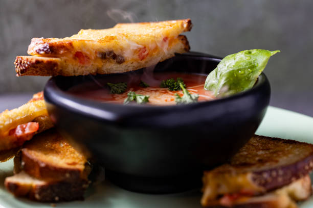 Gourmet Grilled Cheese recipe with tomatoes and ground beef, with Tomato Soup in black bowl garnished with Basil