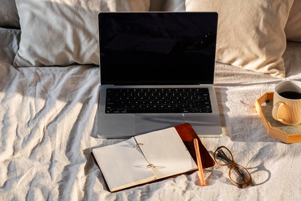 istock Open laptop, blank notebook and eyeglasses on cozy bed. Minimalist workspace vibe ideal for productivity. 2197690302