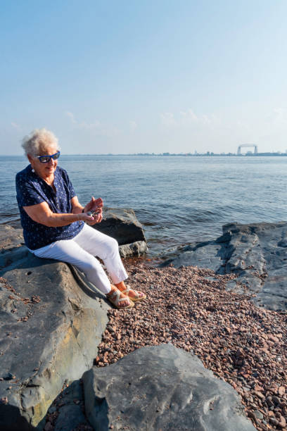 Senior woman sitting on a rocky boulder on the shore of Lake Superior, Dultuth, Minnesota, USA