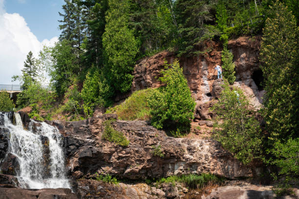 Two brothers climb rocks to explore a cave at the top of Gooseberry Falls, North Shore of Lake Superior, Minnesota, USA