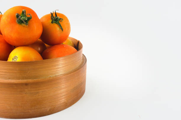A collection of freshly picked ripe tomatoes arranged in a charming wooden basket, captured on a clean white backdrop
