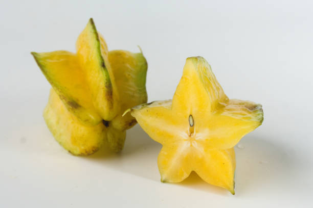 Detailed close-up view of two ripe yellow starfruit showcasing their unique star-shaped design on a clean white background. The vibrant colors highlight their exotic and fresh appearance