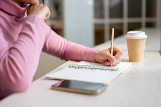 istock A close-up of a woman deep in thought, as she writes in her diary while sitting in a coffee shop. 2197710317