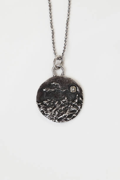 istock Handmade silver round pendant with a mountain range design on a white background with backlight. 2197710592