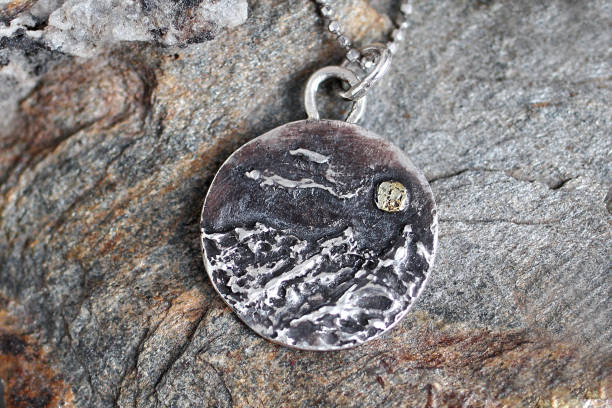 istock Artistically crafted silver mountain pendant with yellow gold moon on a textured stone background. 2197710595
