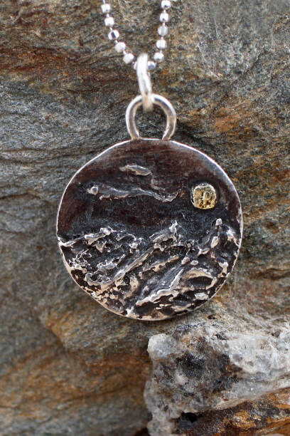 istock Handmade silver pendant with a rough mountains texture and a small gold moon on a silver chain. 2197710602