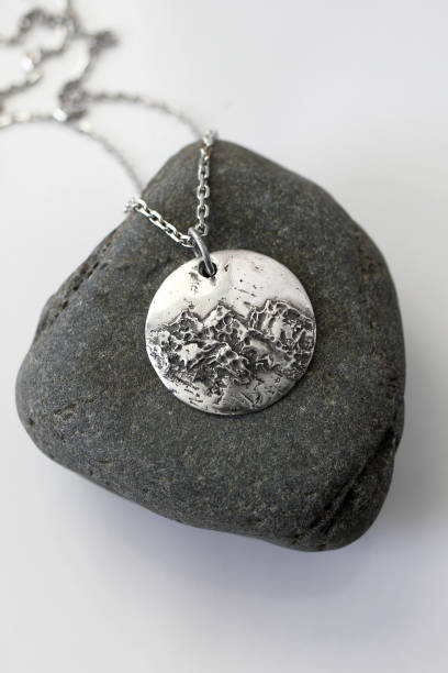 istock Handmade round silver pendant with a unique and textured surface on a rock and white background. 2197710605