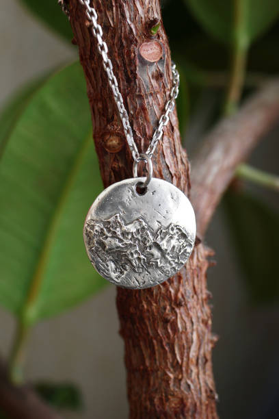istock Unique handmade silver pendant on a silver chain with a textured surface of tree and leaves. 2197710623