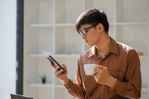 istock Smiling businessman checking phone while holding coffee during break 2197712255