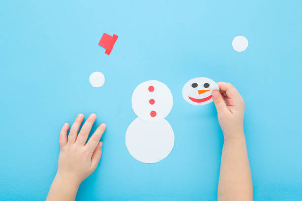 istock Baby boy hands playing and putting together paper snowman puzzle on light blue table background. Pastel color. Homemade jigsaw. Closeup. Point of view shot. Children development. Top down view. 2197717849