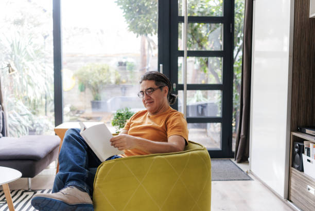 istock Man relaxing in a bright living room while reading a book 2197726303