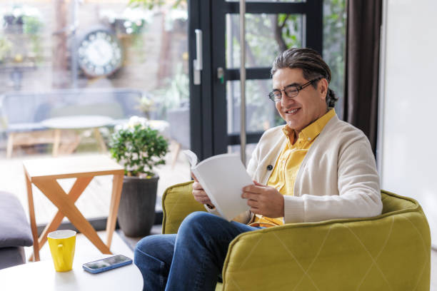 istock Smiling man with book sitting in bright home interior enjoying leisure reading 2197726406
