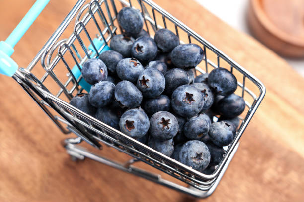 Miniature shopping cart filled with fresh blueberries on wooden background