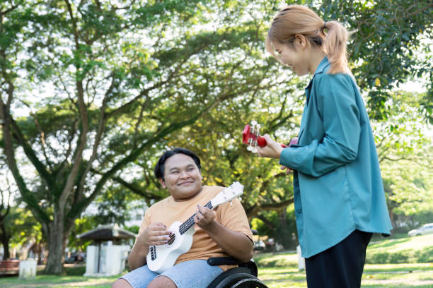 istock Young man in a wheelchair smiling while playing ukulele with a friend. 2197731960