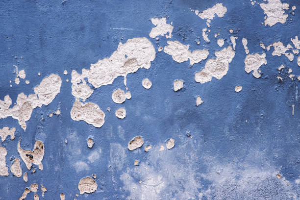 Weathered, peeling blue gray paint on an old concrete wall, revealing underlying bricks. Rough textures, cracks, and faded colors. Copy space