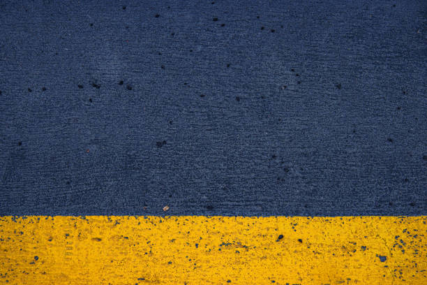 Closeup of a concrete surface featuring a striking yellow stripe on a dark gray asphalt background, ideal for urban, modern, and minimalistic photography themes.  Copy space