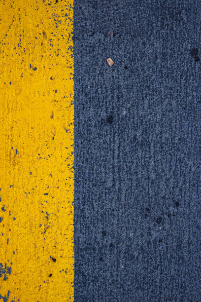 istock Closeup of a concrete surface featuring a striking yellow stripe on a dark gray asphalt background, ideal for urban, modern, and minimalistic photography themes.  Copy space 2197732607