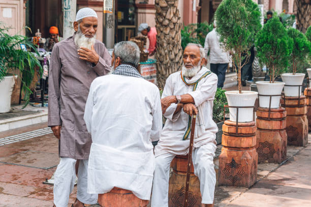 Tangier, Morocco - February 2, 2014: Two men have a rest on a sidewalk outside a mosque, one seats on a vase, the other leans on a small tree. On the wall a holy script from Coran.