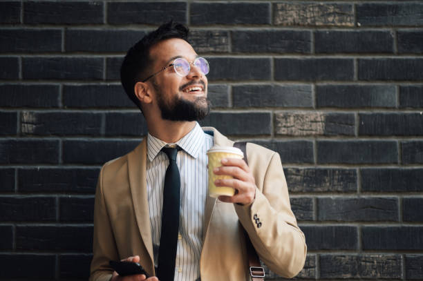 istock Young businessman holding coffee and smartphone looking up smiling 2197738378