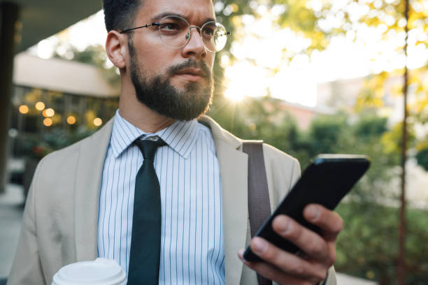 istock Serious businessman using smartphone walking on city street with coffee 2197738698