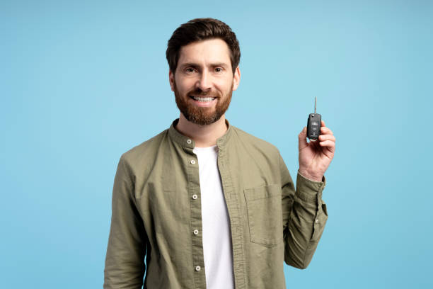 istock Smiling man holding car keys i keyless system isolated on blue background studio 2197740399