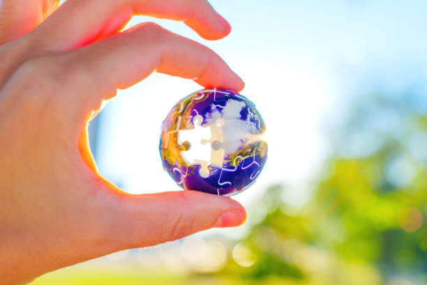 Hand Holding Globe Puzzle Piece Against Blurred Natural Background
