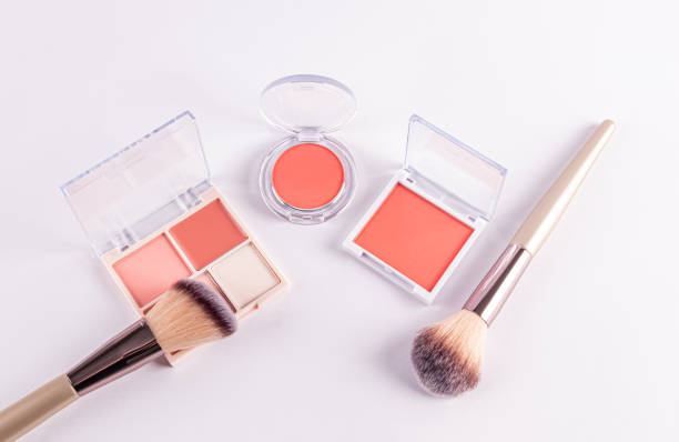 open packs with peach-tone blush and various light tones on a white background with two professional makeup brushes. top view. decorative cosmetics.