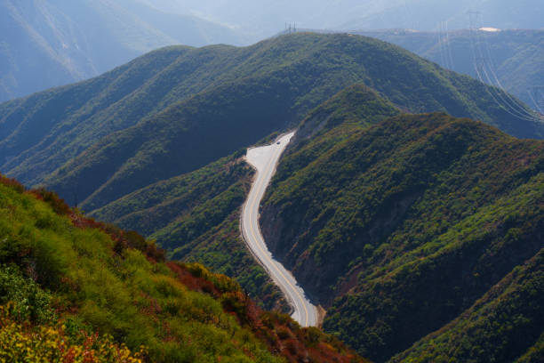 Panoramic view of winding road navigating lush green mountains in Angeles National Forest, Southern California, showcasing picturesque scenery.