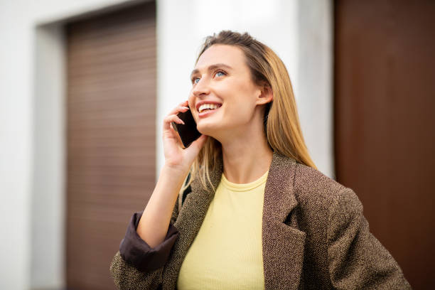 istock Happy young woman looking up while talking on smart phone in city 2197743616