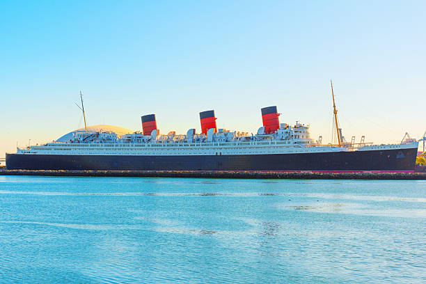 Long Beach, California - January 15, 2025: Historic Queen Mary ship docked in Long Beach Harbor, featuring iconic red and black smokestacks with calm waters.