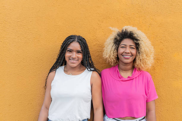 istock Two smiling women posing together against yellow wall 2197747163