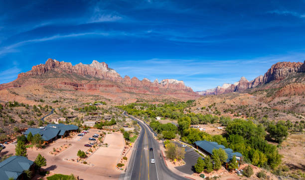 The entrance to the city of Springdale in Utah USA. Behind the city the Zion National Park is seen in the distance, with a scenic road leading toward towering red rock formations. This panoramic view captures the beauty of one of the most iconic landscapes in the American Southwest.