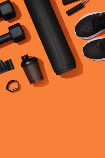 istock Vertical banner with black workout equipment, dumbbells, mat, sneakers, bottle, hand grip on orange background. Fitness, sports items, healthy lifestyle concept. Space for your text 2197750605