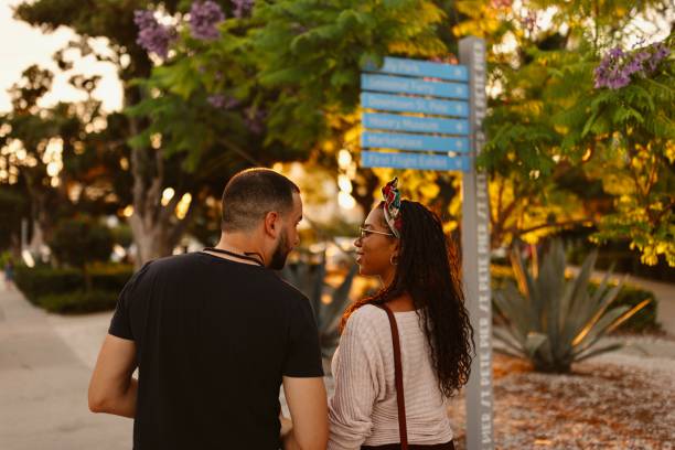 A beautiful young couple is having fun sitting on the street while walking around a Mediterranean town. They enjoy the summer sunny day, holding each other's hand smiling.