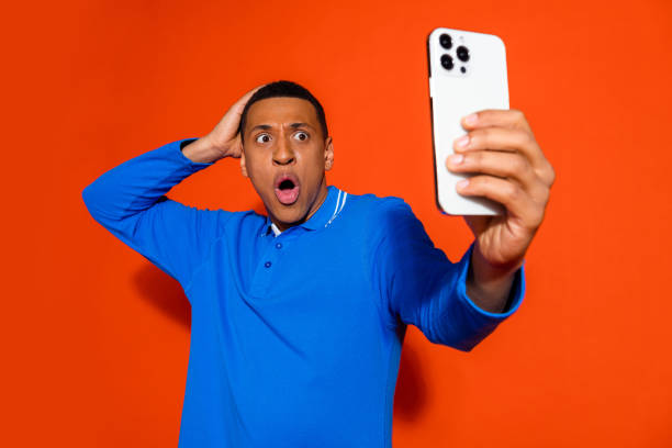 istock Stylish young man surprised taking selfie in blue shirt against orange backdrop 2197756474