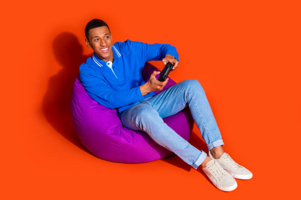 istock Stylish young man enjoying leisure time with video game on orange background 2197757620