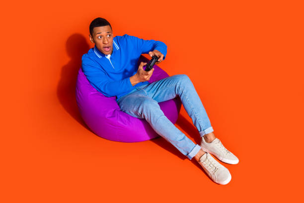 istock Stylish young man enjoying a video game on orange background 2197757731