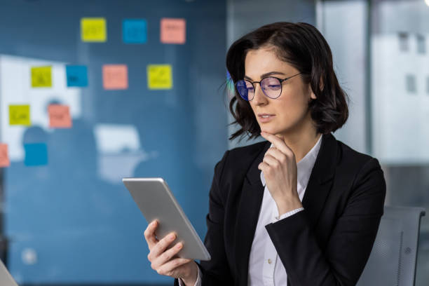 istock Confident businesswoman wearing glasses using a tablet in a modern office, surrounded by colorful sticky notes, showcasing professional engagement and technology in work environment 2197764754