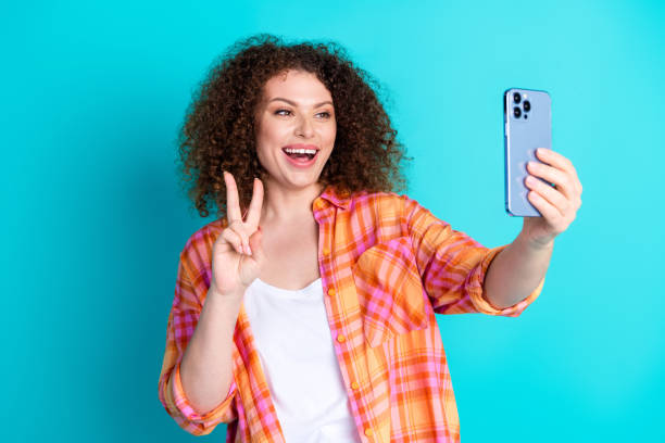istock Happy young woman taking a selfie on turquoise backdrop with peace sign gesture 2197764857
