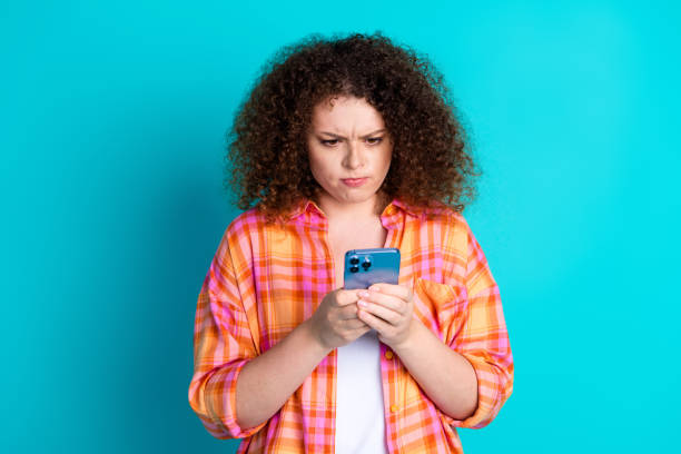 istock Curly-haired woman using smartphone against a vibrant teal background displaying a thoughtful expression 2197765024